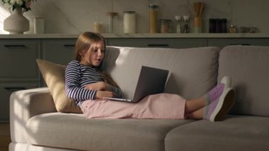 Kanepede uzanan küçük kız rahat rahat film dizüstü bilgisayar izliyor hafta sonu rahatına bakıyor çocuk gülüşü, eğlence aleti, internet aletleri, eğlenceli kadın videoları.