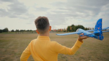 Arkaya bakan sevimli çocuk beyaz oğlan oğlan oğlan oğlan okul çocuğu oyuncak uçakla dışarıda güzel doğa parkı sahasında koşuyor. Kaçma oyunu oynayan çocuk uçan uçak hayali kuruyor pilot oluyor.