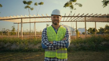 Portre başarılı bir şekilde gülümseyen beyaz, erkek, ekoloji mühendisi, ziraat mühendisi üniformalı adam inşaat dışında kameraya bakarak el sıkıştı. Tarım eko tarım işi