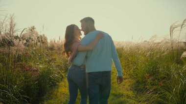Arkaya bakan mutlu bir aile, beyaz, evli, sevgi dolu bir çift, bir kadını öpüyor, sarılıyor, sarılıyor. Romantik eşler el ele tutuşur karı öper güneşli sabah kırsal çayırlarda dolaşırlar