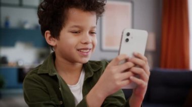 Afro-Amerikalı etnik çocuk çocuk çocuk mutlu gülümsüyor cep telefonu akıllı telefon kullanarak evde oyun oynayan kullanıcıda sosyal medya yazarak internet oyunu cep telefonu oyun uygulaması bağımlılığı oynuyor