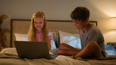 Mutlu Kafkas gevşemiş genleri küçük çocuklar küçük kız çocuk gülümseyen oğlan çocuk birlikte film izlemekten hoşlanan gece çizgi filmi bilgisayar bilgisayarı laptop cihazlı yatak odası pijama partisi.