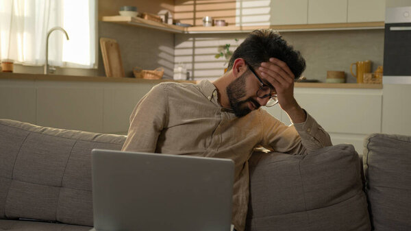 Шокированы расстроен индийский арабский мужчина парень деловая работа из домашней кухни отрицательный результат беспокоился, что обеспокоенный мужчина фрилансер на диване читать ноутбук уведомления компьютерная проблема неудача сложный кризис