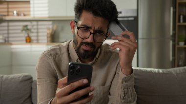 Stresli Arap Hindistanlı adam, üzgün erkek kart sahibinin cep telefonuyla internet üzerinden ödeme yapmasına hayal kırıklığına uğramış bankacılık uygulaması hatası para dengesi ve finansal limit eksikliği nedeniyle hayal kırıklığına uğramış.