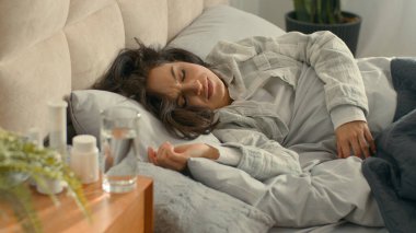 Yatakta uzanan kadın karın ağrısı, regl dönemi, kadın hapları, sağlıksız zehirlenme, hasta karın ağrısı, karın ağrısı, ağrı kesici, ev hapları.