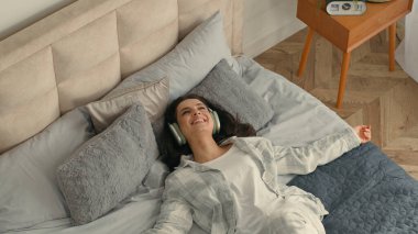 Genç, mutlu, esmer bir kadın, yatağında kulaklık takıp müzik dinliyor. Akıllı telefon teknolojisi kullanıyor. Keyifli, rahat, rahat, rahat bir kız.