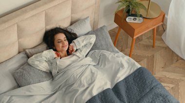 Mutlu bir kadın, yatağında uzanıyor, tembel bir kız. Rahat bir otel odasında dinleniyor. Gülümsüyor, keyifleniyor, uykulu bir yatak odasında keyif çatıyor.