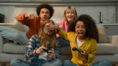 Konsol oyunu oynayan Afrikalı Amerikalı bir kadın hile yapıyor. Kafkasyalı bir erkeğe göz kulak ol. Başarısız olan erkek.