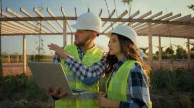 İki Kafkas deneyimli mühendis kadın kadın erkek erkek erkek erkek kasketli dizüstü bilgisayar kullanarak inşaat projesinin stratejisini tartışıyorlar online teknoloji parkını inceliyorlar.