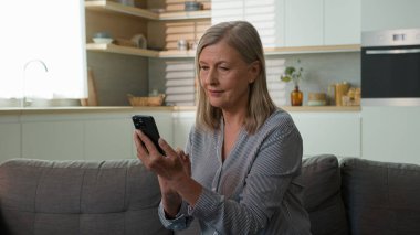 Gülümseyen olgun Kafkasyalı yaşlı kadın yaşlı, büyük anne, ekranda yazı yazan, cep telefonu kullanan, internetten kıyafet seçen, yaşlı, internet kullanan, bankacılık uygulaması kullanan yaşlı kadın.