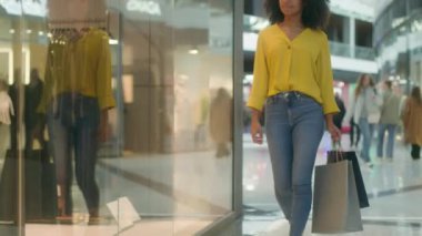 Genç Afro-Amerikan mutlu kadın alışveriş merkezine gidiyor alışveriş kolikleri özel moda paketleri taşıyor. Vitrin butiği arıyor. Yeni manken koleksiyonu siyah cuma tüketicisini seçin.