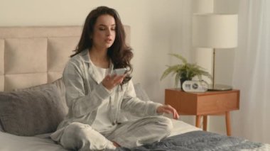 Beyaz Avrupalı bir kadın yatağında rahat bir hafta sonu geçirmek için oturuyor. Cep telefonunu açıyor. Telefon görüşmeleri yapıyor.
