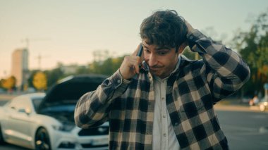 Stresli şoför Kafkasyalı adam konuşuyor. Cep telefonundan araba servisini arıyor. Açık yolda duruyor.