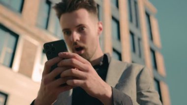 Şaşırmış Kafkasyalı adam açık havada telefonla e-posta alıyor. Erkek işadamı şoke oluyor. İnternette sosyal ağda haber okuyor.