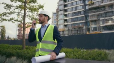 Şehir geliştirme binaları elektrik mühendisliği Kafkasyalı adam güvenlik şapkalı mühendis çelik yelek üniformalı sıkı adam telsiz planıyla konuşuyor.