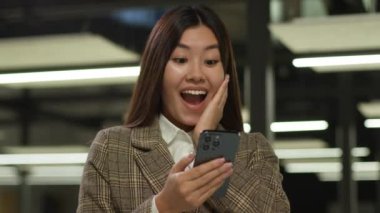Çok neşeli Asyalı iş kadını elinde cep telefonu olan Koreli kız akıllı telefon zaferiyle başarı kazandı. Japon iş kadını Çinli kadın ofiste harika bir iyi haber mesajı okuyor.