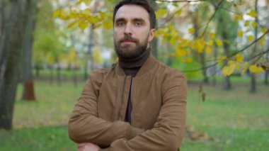 Ciddi yakışıklı, kendine güvenen, bin yıllık yetişkin bir adam güz mevsiminde güçlü poz veriyor. Kendine güveni tam 30 'lu yaşlarda erkek. Göğsüne yaslanmış.