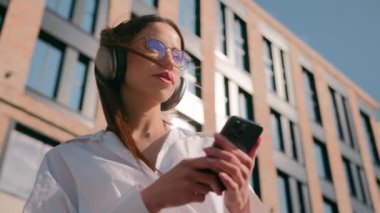 Kulaklıkla müzik dinleyen kaygısız İspanyol kadın şehir güneşinde mobil ses uygulaması kullanıyor rahatlamış kız iş kadını öğrenci sokakta mp3 'ün keyfini çıkarıyor.