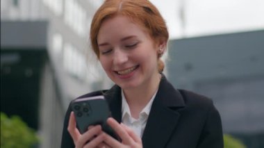 Gülümseyen mutlu, genç, beyaz, kadın, iş kadını, cep telefonu internet uygulaması, mesajlaşma, kahkahalar, akıllı telefon sosyal medyası, açık şehir caddesi.