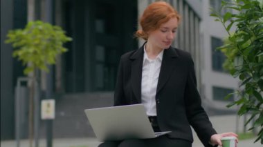 Genç, mutlu, Kafkasyalı örnek iş kadını, kızıl, kadın, internette bilgisayar kullanarak bilgisayar başında oturmuş, internet üzerinden sohbet ediyor, belediye binasının önünde kahve içiyor.