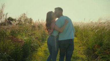 Arkaya bakan mutlu bir aile, beyaz, evli, sevgi dolu bir çift, bir kadını öpüyor, sarılıyor, sarılıyor. Romantik eşler el ele tutuşur karı öper güneşli sabah kırsal çayırlarda dolaşırlar
