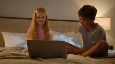 Mutlu Kafkas gevşemiş genleri küçük çocuklar küçük kız çocuk gülümseyen oğlan çocuk birlikte film izlemekten hoşlanan gece çizgi filmi bilgisayar bilgisayarı laptop cihazlı yatak odası pijama partisi.