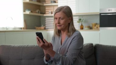 Gülümseyen olgun Kafkasyalı yaşlı kadın yaşlı, büyük anne, ekranda yazı yazan, cep telefonu kullanan, internetten kıyafet seçen, yaşlı, internet kullanan, bankacılık uygulaması kullanan yaşlı kadın.