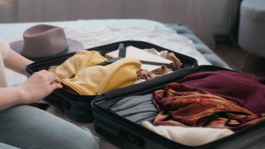 Tanımlanamayan bir kadın seyahate çıkmaya hazırlanıyor. Turizm turizmi hazırlığı. Evde tatil için giysi valiziyle birlikte valize yılanı yapıştırın.