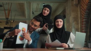 Arap mutlu iş adamı görüntülü konuşma video konferansı grafikler, belgeler iş sunumu tesettürlü Müslüman kadın tesettüre katılan iş arkadaşları ofiste iş birliği yapıyor.
