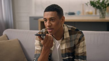 Mutlu Afrikalı Amerikalı adam kanepe koltuğunda. Çift ırklı erkek. Cep telefonu kullanıyor. Sesli mesaj kaydediyor.