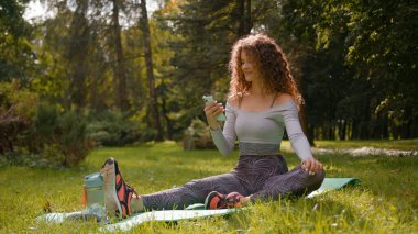 Beyaz kadın sporcu kız fitness bayan park doğasında şehir dışında yoga minderinde dinleniyor cep telefonu akıllı telefon bağımlılığı tarayıcı uygulaması kullanıyor çevrimiçi sohbet etkilici seçin
