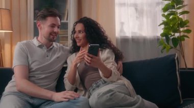 Mutlu çift, beyaz erkek, erkek, erkek, erkek, İspanyol kadın, kız, kız, gülümseyen kız, kanepede birlikte alışveriş yaparken internetten cep telefonu alışverişini tartışır.