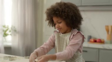 Afro-Amerikalı küçük tatlı kız 10 'lu yaşlarda, çocuk, çocuk, çocuk, çocuk evlat edinme, çocuk, mutfakta tek başına yemek pişirme bisküvi fırını, çiğ buğday hamuru biçimli kurabiye bıçağı.