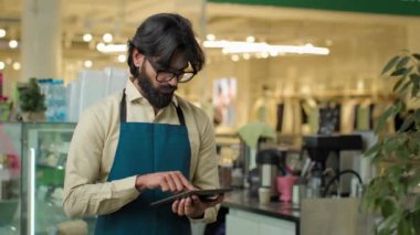 Kafedeki Hintli erkek garson internet hizmeti kullanarak dijital tablet kafeterya çalışanı Arap barista adam dijital tablet siparişi yazarak kablosuz bilgisayar küçük işletme menüsünü yönetiyor.