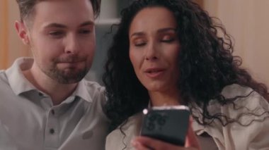 Çok ırklı çift, beyaz erkek, erkek, erkek, erkek, erkek, kadın, Latin, kız, kız, cep telefonu kullanıyor. Evde akıllı telefon alışverişini tartışıyorlar.