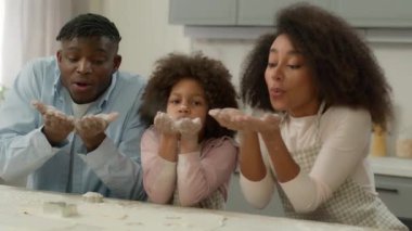 Mutlu Afro-Amerikan aile babası, erkek kadın anne, mutfakta oyun oynuyorlar küçük kız çocuk, beyaz un tozuyla oynuyorlar yemek pişiriyorlar, alkışlıyorlar.