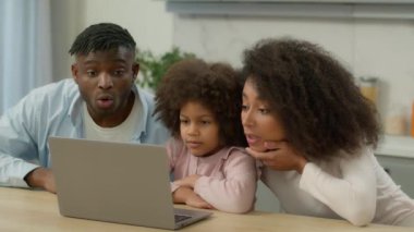 Afrika kökenli Amerikalı etnik aile babası baba kadın anne ve küçük kız çocuğu dizüstü bilgisayar kullanan kız çocuğu şaşırttı iyi haber kazandı bilgisayar kazandı ev mutfağında bağırdı