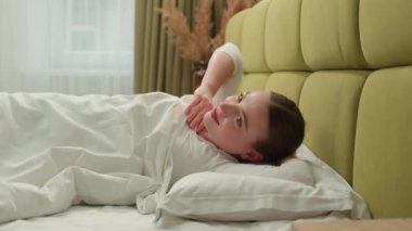 Mutlu, sağlıklı, beyaz bir kadın sabah uyanıyor. Daire otel odasının yatak odasında, rahat bir uyku uykusunda uyanıyor. Rahat uyuyan, esneyen bir kadın.