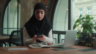 Müslüman İslami tesettüre giren iş kadını iş kadını dizüstü bilgisayarda çalışan ofis çalışanı cep telefonuna mesaj geldi.