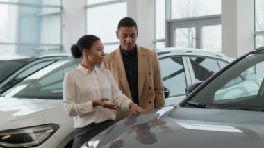 Afro-Amerikalı kadın yönetici tüccar satıcı kadın satıcı kadın araba galerisindeki yeni modern elektrikli araba kiralama servisini seçen adamı gösteren müşteriye danışmaya yardım ediyor.