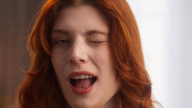 Çekici mutlu beyaz kadın kaygısız bayan güzel bayan kameraya bak neşeli jest duygu işareti büyüleyici kızıl saçlı kız gülümsemesi mükemmel beyaz dişlerle evde poz veriyor.