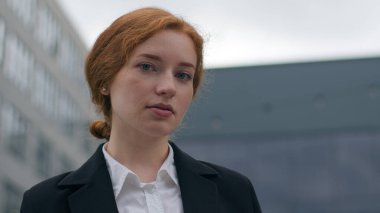 Kendine güvenen, başarılı, genç, beyaz, kızıl saçlı, mutlu, iş kadını, zarif, resmi giyinmiş, şehir merkezindeki kameraya benzeyen bir kız. İş başarısı hedefleri