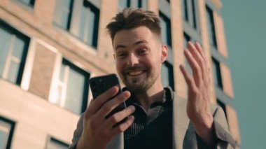 Mutlu Kafkas erkek işadamı online kazanan e-posta okuyucu iyi haberleri kontrol ediyor şehir dışında ofis merkezinin yakınında akıllı telefon kullanarak zaferi telefonla kutluyor.