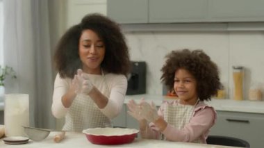 Afro-Amerikan ailesi hamurlu pizza tarifi yapar. Anne kadın, küçük kıza gülümsemeyi öğretir. Kirli un el çırpmayı, mutfakta avuç içlerini alkışlamayı öğretir.