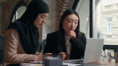 İki kadın çok ırklı iş kadını patron iş kadını Asyalı kadın Arap Müslüman iş kadını tesettürde çalışıyor veri bilgisayarı belgelerini analiz ediyor ofis konuşmalarıyla sonuçlanıyor