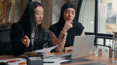 Kadın iş arkadaşları çok ırklı iş kadınları Asyalı kadın Arap Müslüman iş kadını tesettürde bilgi dizüstü bilgisayarı işbirliği hakkında görüştüler ofis konuşmasında not defteri yaz