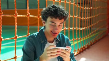Gadget, gülümseyen, beyaz tenli, genç, erkek öğrenci üniversite okulunda cep telefonu oyunu oynayan erkek öğrenci akıllı telefon bağımlısı eğitim molası verdi.