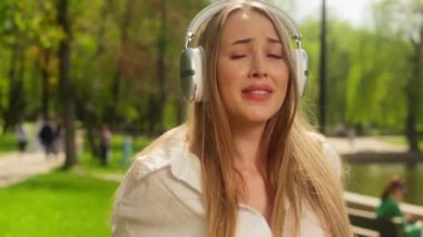 Avrupalı bir kadın müzik kulaklığı dinliyor, şarkı söylüyor, gülümsüyor, neşeli bayan mutlu kız pozitif enerji dolu haftasonu kulaklıkları dışarıda dans eden neşeli eğlence teknolojisi.