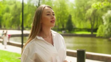 Avrupalı mutlu kadın parka bakıyor. Kız arkadaşlarıyla buluşuyor. El sallıyor, gülümsüyor.