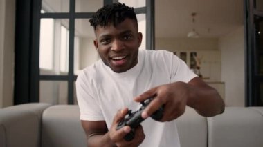 Afro-Amerikan mutlu adam bağımlı erkek oyuncu kanepe internet oyun bağımlısı oyun konsolu çevrimiçi video oyunu oynayan adam uzaktan kumandalı eğlence hafta sonu kumandası kullanarak joystick 'i tutun